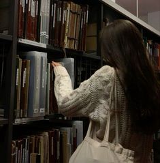 a woman is picking up some books from a book shelf in a library with several shelves full of books