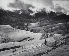 black and white photograph of rolling hills with clouds in the sky over them on a cloudy day