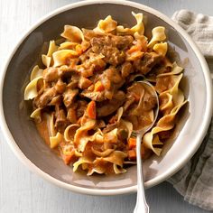 a white bowl filled with pasta and meat on top of a table next to a napkin