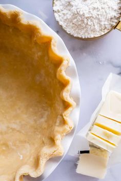 an uncooked pie crust next to butter and other ingredients on a marble table