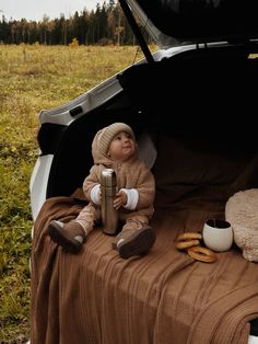 a baby doll sitting in the trunk of a car with its hood open and food on the ground