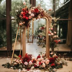 a mirror sitting on top of a table covered in flowers and greenery next to a window