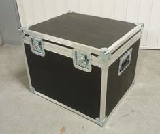 a black and silver trunk sitting on top of a cement floor next to a white wall