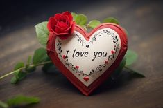 a red rose sitting on top of a wooden table next to a heart shaped box