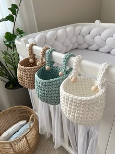 three crocheted baskets hanging on the side of a white rail next to a plant