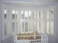 a baby crib in the corner of a room with white shutters