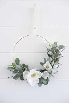 a wreath with white flowers and greenery hanging on a wall