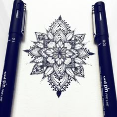 two pens sitting next to each other on top of a piece of paper with an intricate design