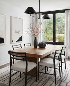 a dining room table with chairs and a vase on top of it in front of a large window