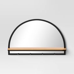 an oval mirror with a wooden shelf underneath it on a white wall behind the mirror is a light wood and black metal frame