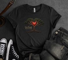 Embrace the power of transformation with our 'Grow Through What You Go Through' Inspirational Quote T-Shirt, featuring a surreal image of a tree with roots intertwined around a glowing heart. This design symbolizes the resilience and strength that comes from overcoming challenges, with the phrase 'Grow Through What You Go Through' reminding you that growth often arises from adversity. Perfect for those who value inspiration, motivation, and mental health awareness, this tee is both powerful and thought-provoking. Crafted from premium Bella + Canvas 3001 fabric, this t-shirt offers a soft, comfortable fit, ideal for moments of reflection or sharing a message of resilience. Whether you're navigating personal challenges or supporting someone else's journey, this shirt is a beautiful expressio Tree With Roots, Glowing Heart, Message T Shirts, Overcoming Challenges, Health Awareness, Mental Health Awareness, Tree Art, Inspirational Quote, Thought Provoking