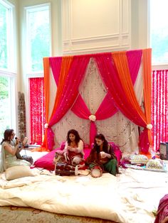 two women sitting on a bed with pink and orange drapes