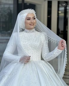 a woman in a white wedding gown and veil posing for the camera with her hands on her hips