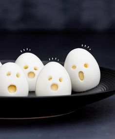 some white eggs with holes in them on a black plate and one has yellow eyes