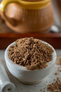 a white bowl filled with brown powder next to a measuring cup and spoon on a table