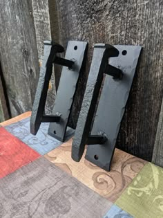 two metal hooks are on the side of a wooden fence with colorful fabric behind them