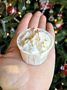 a hand holding a small cupcake in front of a christmas tree