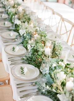 a long table with white plates and greenery