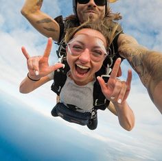 a man and woman are skydiving in the air with their hands up while making peace signs