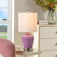 a purple lamp sitting on top of a table next to a pink chair