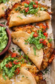 several tortillas with guacamole and salsa on top, sitting on parchment paper