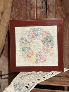 a wooden frame with a white doily on top of it next to a piece of cloth