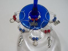 a blue wine glass holder with beads and charms hanging from it's side on a white table