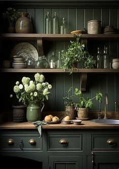 a kitchen with green cabinets and flowers on the counter top in front of an open shelving unit