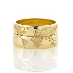 two gold wedding bands with the world map on them, set against a white background