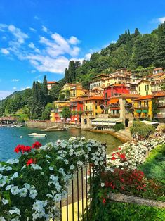 colorful houses on the shore of a lake surrounded by greenery and flowers, with mountains in the background