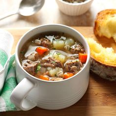 a bowl of soup next to a roll on a cutting board