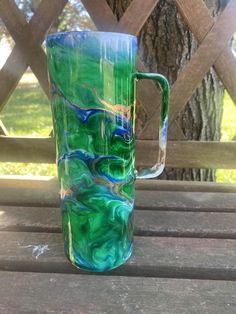 a green and blue mug sitting on top of a wooden table next to a tree