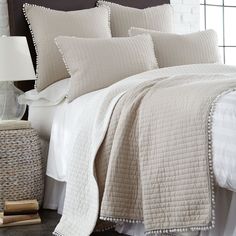 a bed with white sheets and pillows in a bedroom next to a basket on the floor