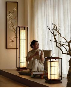 a woman sitting on the floor next to two lamps and a vase with flowers in it