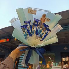 a person holding up a bunch of chocolates in front of a building with a blue ribbon