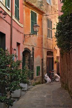 an alley way with several buildings and green shutters on either side, one building has two balconies