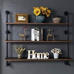 three shelves with books, vases and flowers on them in front of a gray wall