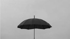 a black and white photo of an umbrella on a pole in the rain, against a gray sky