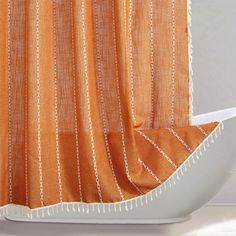 an orange shower curtain with white trim on the bottom and side, in front of a bathtub