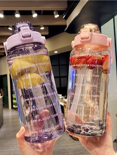 two people holding up water bottles with strawberries, lemons and blueberries in them