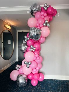 a bunch of pink and silver balloons hanging from the side of a wall next to a mirror