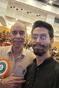 two men standing next to each other in front of an auditorium full of people holding cell phones