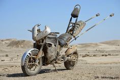 an old dirt bike is parked in the middle of the desert, with metal parts attached to it