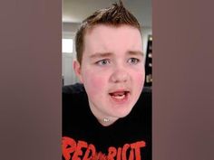 a young boy making a funny face while wearing a red riot t - shirt and looking at the camera