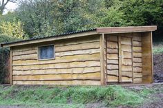 a small wooden building sitting on top of a grass covered field next to trees and bushes