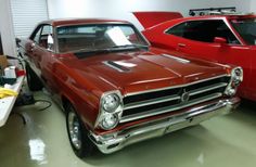 an old red car parked in a garage next to another classic car on the floor