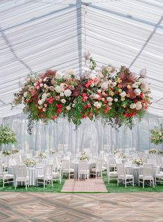 an outdoor tent with tables, chairs and flowers hanging from the ceiling