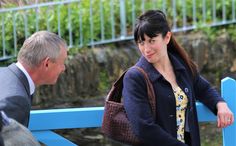 a woman standing next to a man on a blue bench near a fence and water