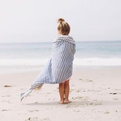 a person standing on the beach with a towel wrapped around their shoulders and looking at the ocean