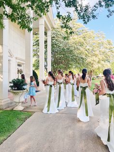 a group of women in white dresses standing on the side of a building with green sashes